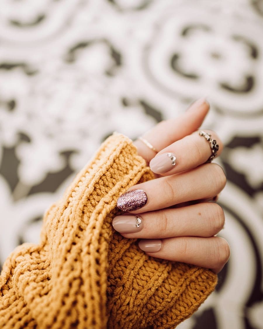 Unhas nude com glitter e strass, mão sobre tricô mostarda